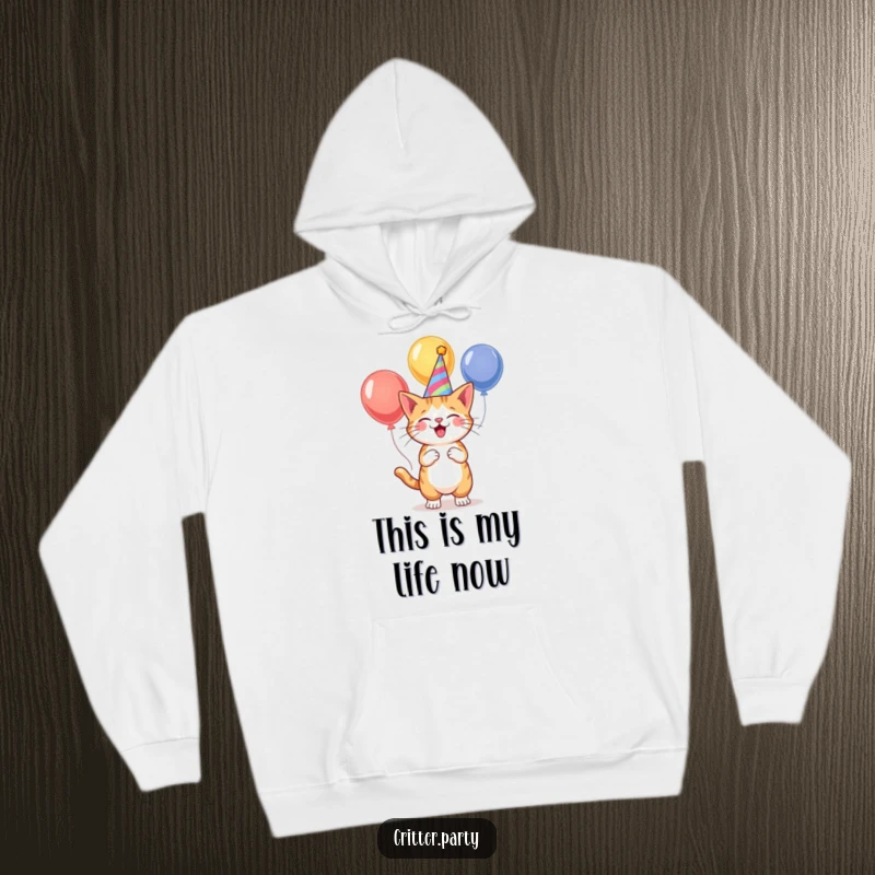 Funny, festive cat in a party hat, juggling colorful balloons, featured on a soft, warm hoodie for cozy, humorous vibes.